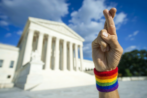 Gay person with fingers crossed in front of the Supreme Court