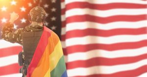 US Flag in background with solider wrapped in gay flag faces it.